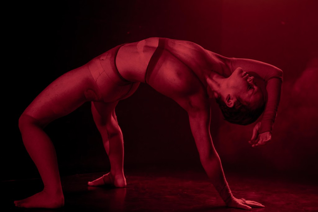 Un danseur exécutant une pose expressive sur fond rouge, mettant en valeur la technique et la fluidité du mouvement.